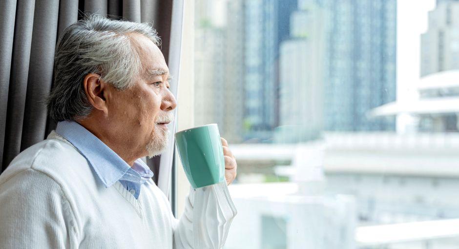 Asian man looking out the window while drinking coffee