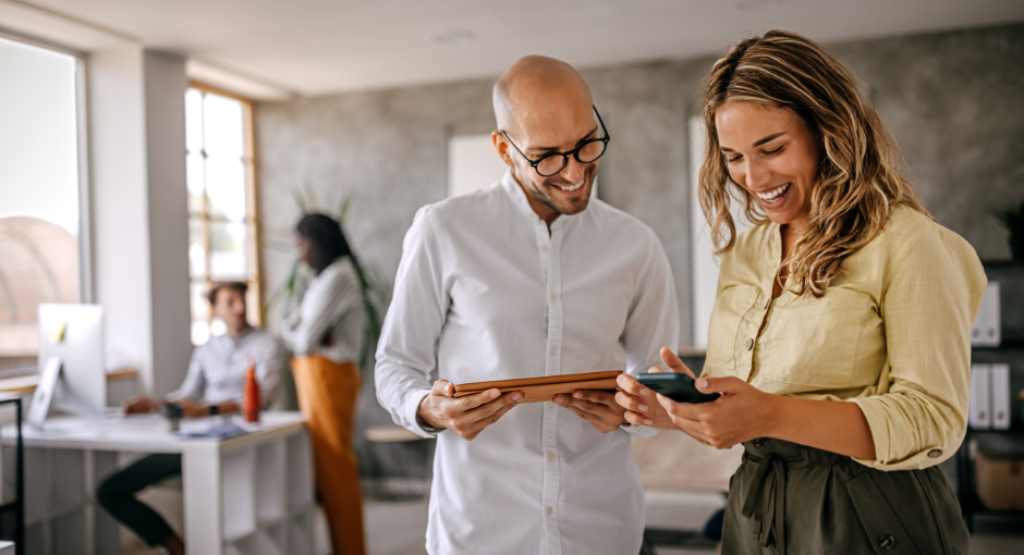 Employee showing boss something on her phone while he's holding an ipad smiling