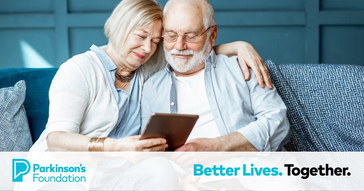 A woman hugging a man on a couch, both looking at a tablet.