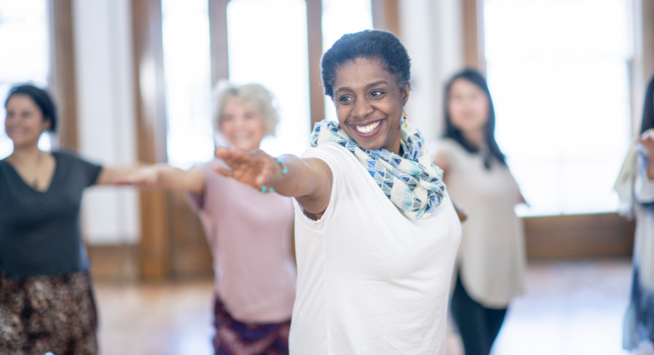 Women attending indoor group exercise class with arms outstretched. 