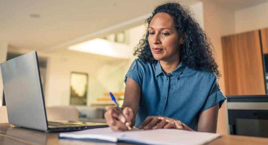 Woman writing notes while looking at laptop