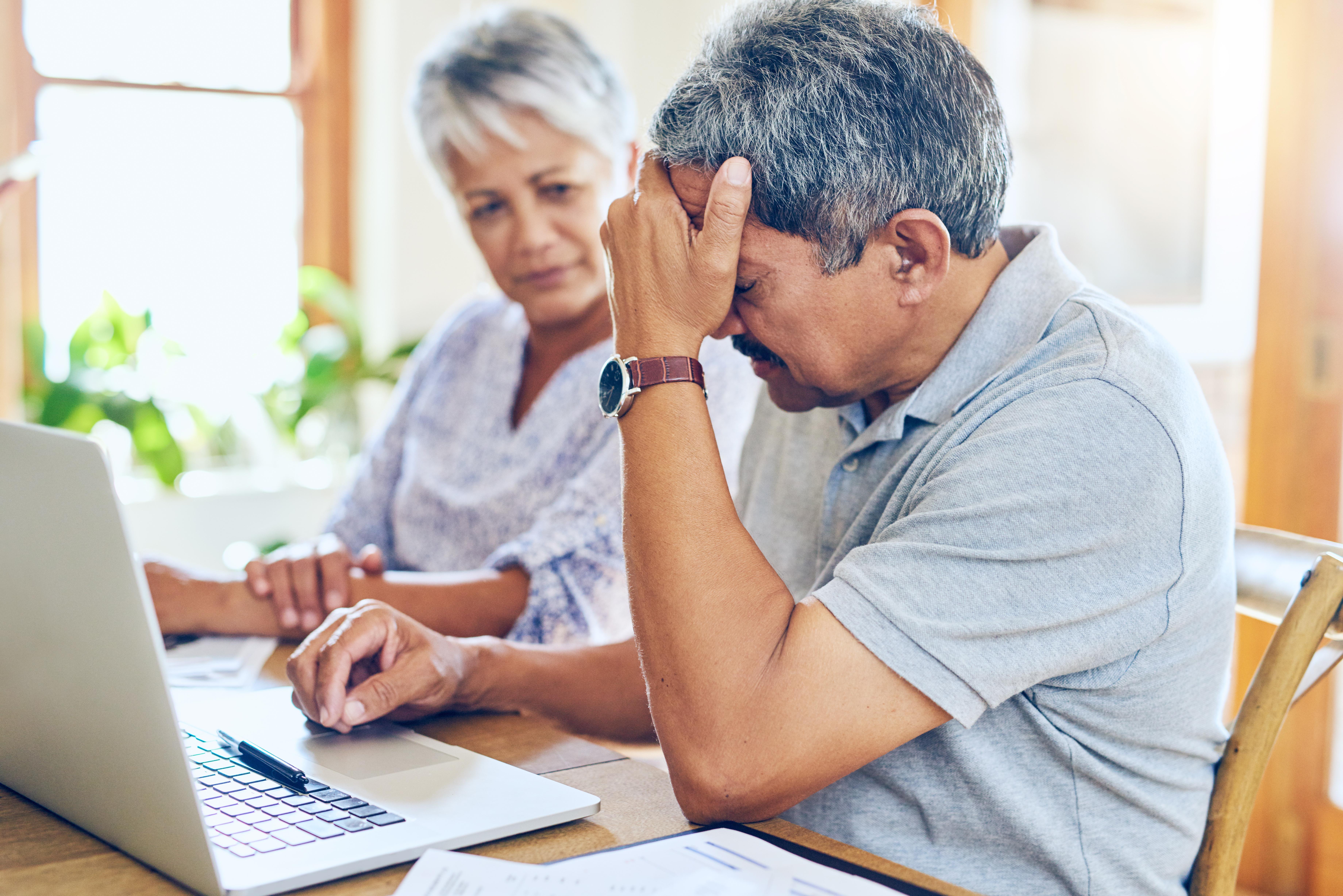 Husband frustrated while looking at laptop and wife comforting him