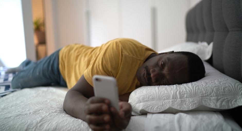 Man laying on bed looking at phone with sad expression