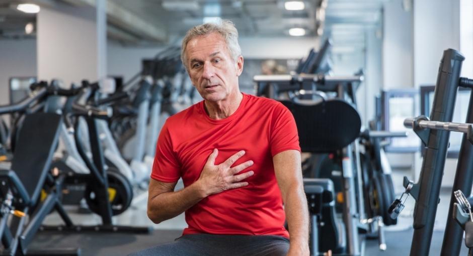 Man at indoor gym, struggling to breathe with hand on chest