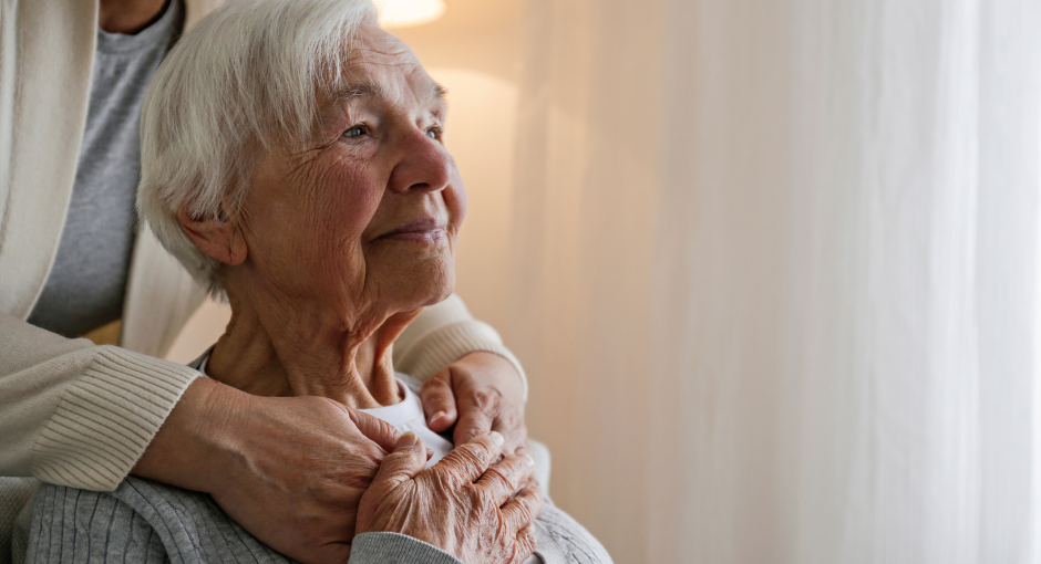 an elderly mother looking off in the distance while being hugged by her daughter not in the frame