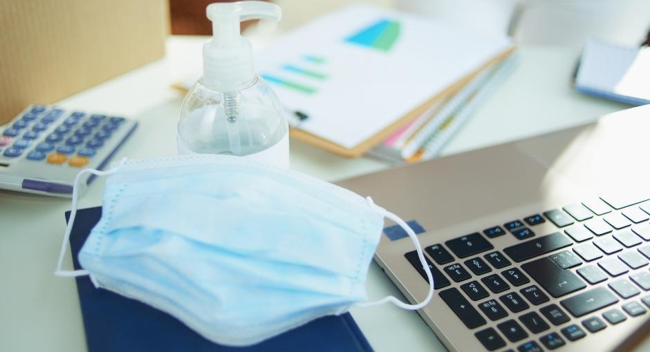 Face mask on a desk near laptop and hand sanitizer