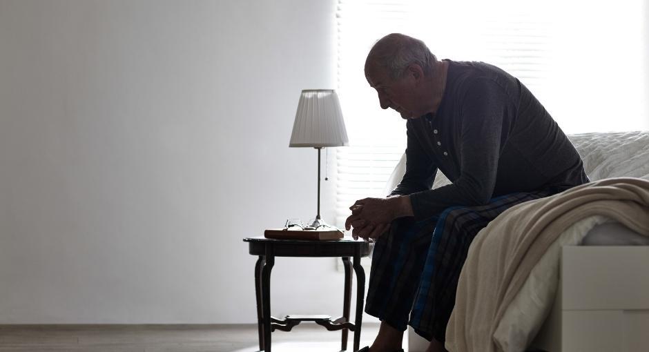 Man crouched over sitting on bed