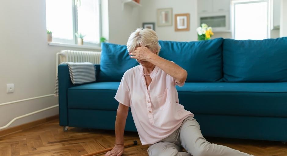 Woman sitting on floor in front of couch with left hand over eyes, indicating dizziness
