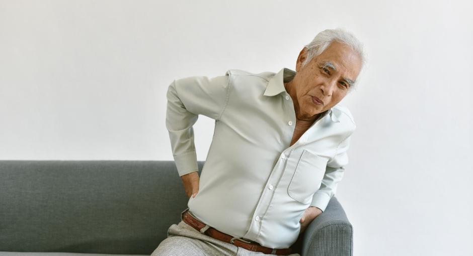 Man sitting on couch with pained expression and holding his back with both hands