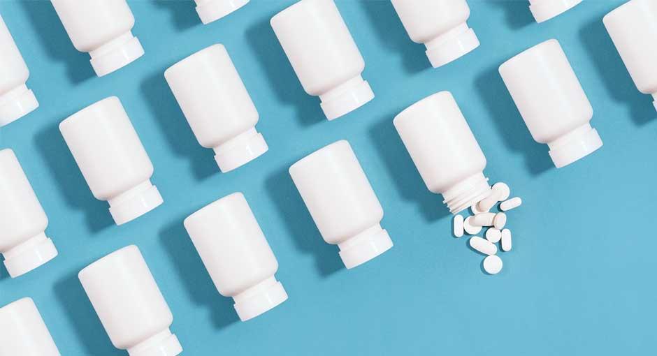 White pill bottles arranged in an organized fashion on a blue background with one bottle spilling pills