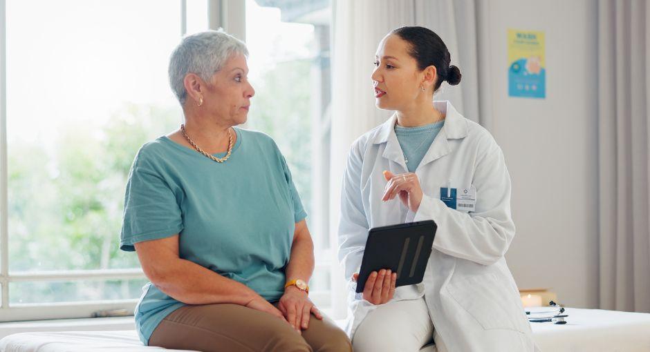A female patient talking with her doctor who is holding a tablet.