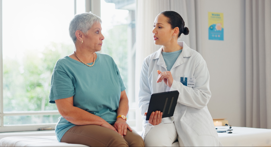 A female patient talking with her doctor who is holding a tablet.