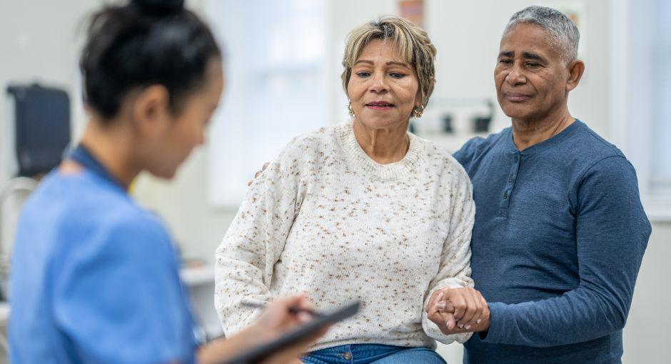 La paciente se sienta en la camilla de exploración con su marido cerca.