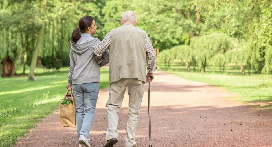 Woman linking arms with man using cane walking in a park