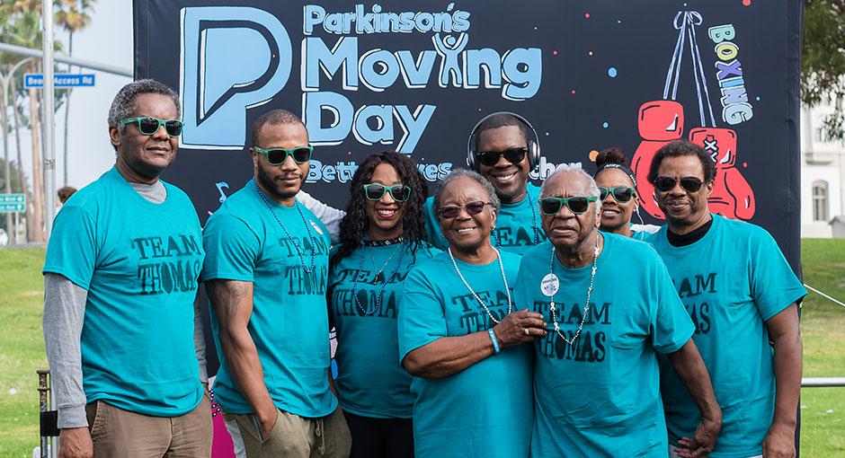 Moving Day banner - Multigenerational family standing in front of a hand-drawn Moving Day logo at the Parkinson's Foundation walk
