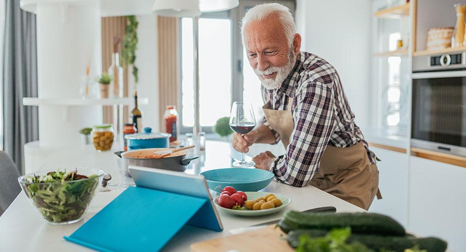Older man taking an online cooking course while relaxing and drinking wine