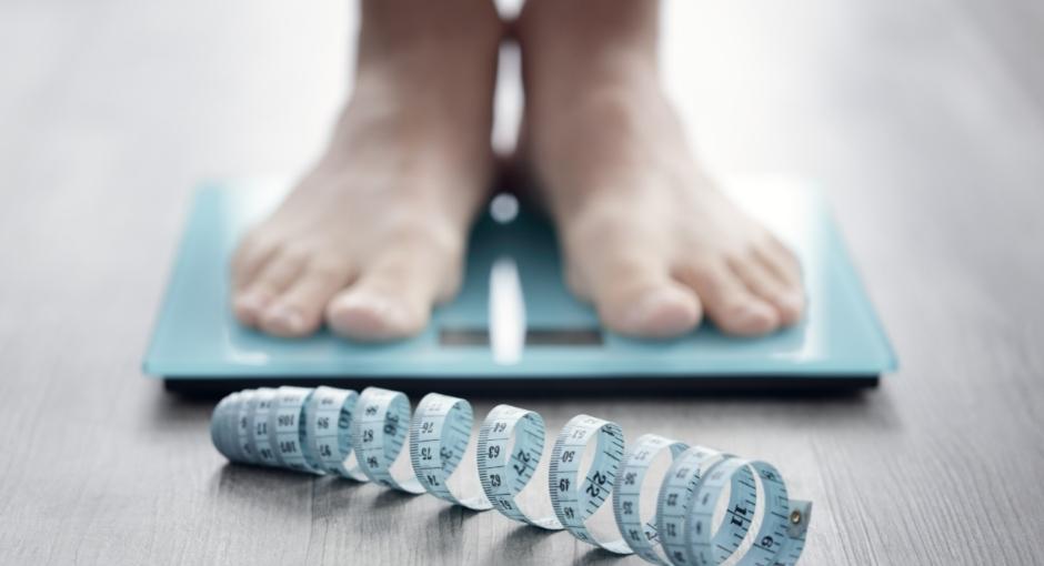 Person's feet standing on weight scale with tape measure on floor